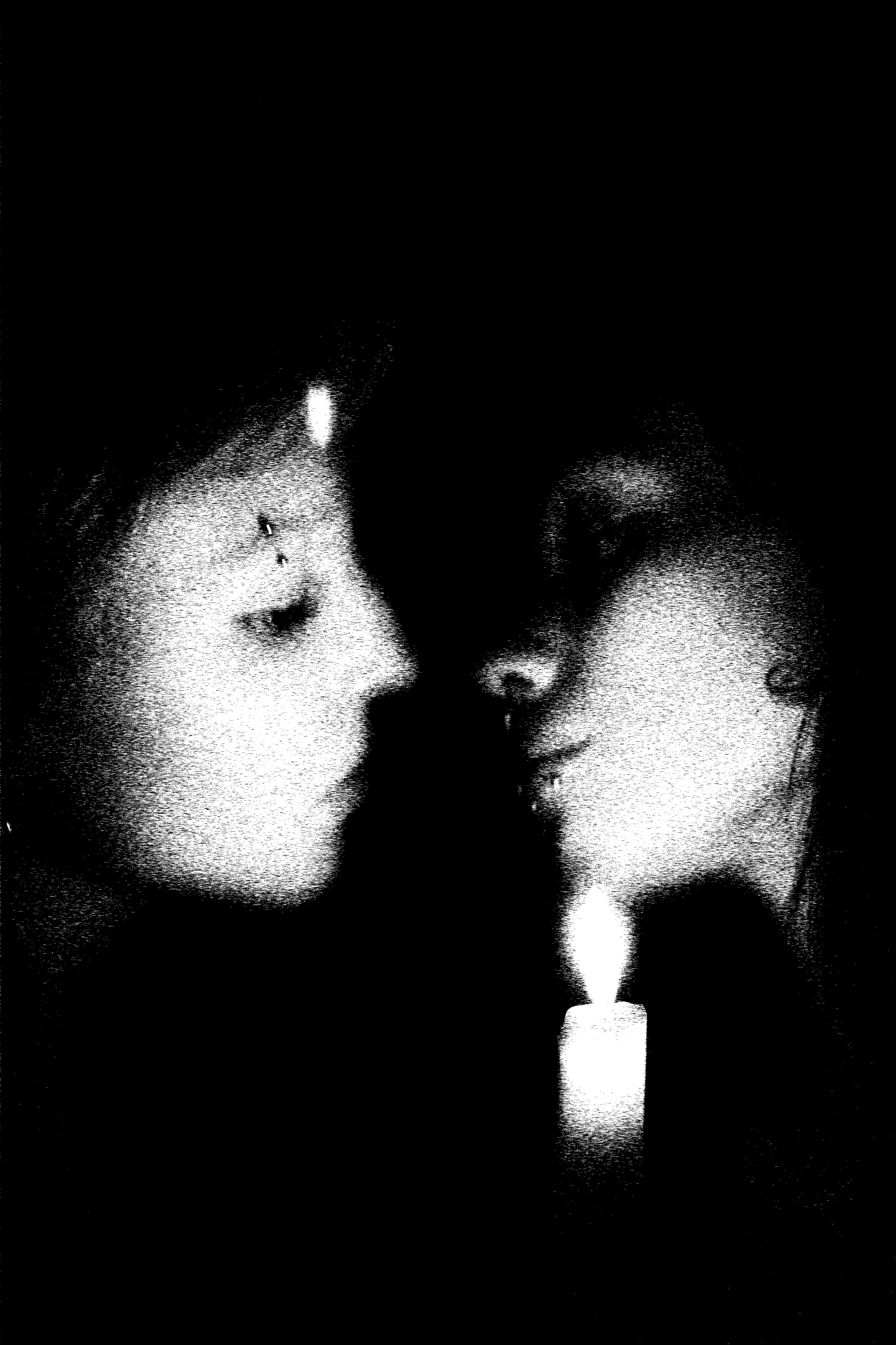Two models face each other in near darkness, lit only by a single candle.